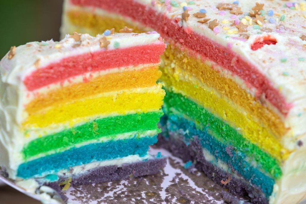 Rainbow cake with the white cream topping cut into two slices